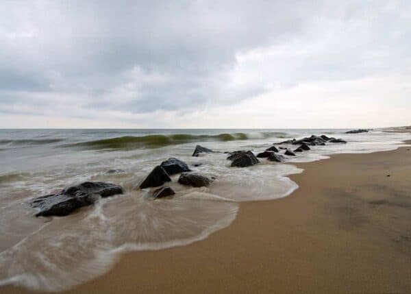 Stille morgen ved havet, bølgerne slår sagte ind på stranden hvor der tegnes silkebløde silhoutter i sandet fra vandets skum