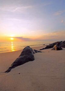 Smuk aften ved havet, de sidste solstråler spejler sig gennem havet helt mod kysten, lyser reflekteres smukt i stenene på stranden
