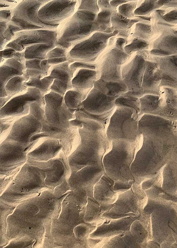 Lyset leger i de fantastiske mønstre i sandet på stranden