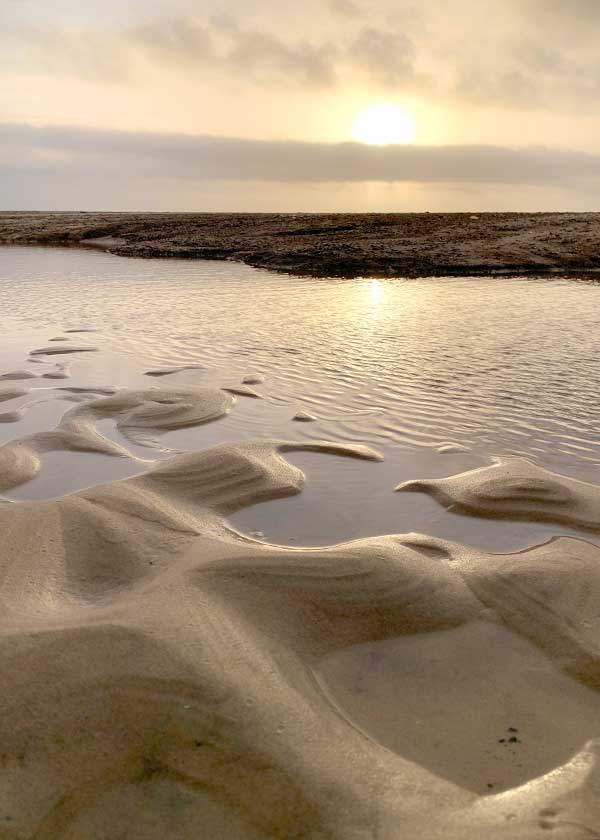 Solnedgang på stranden - lyset spiller i indsøen og sandet former flotte mønstre