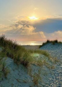 Solen trækker sin stråler gennem skyerne, og tegner et fantastisk scenarie på himlen med klit og strand som baggrund.