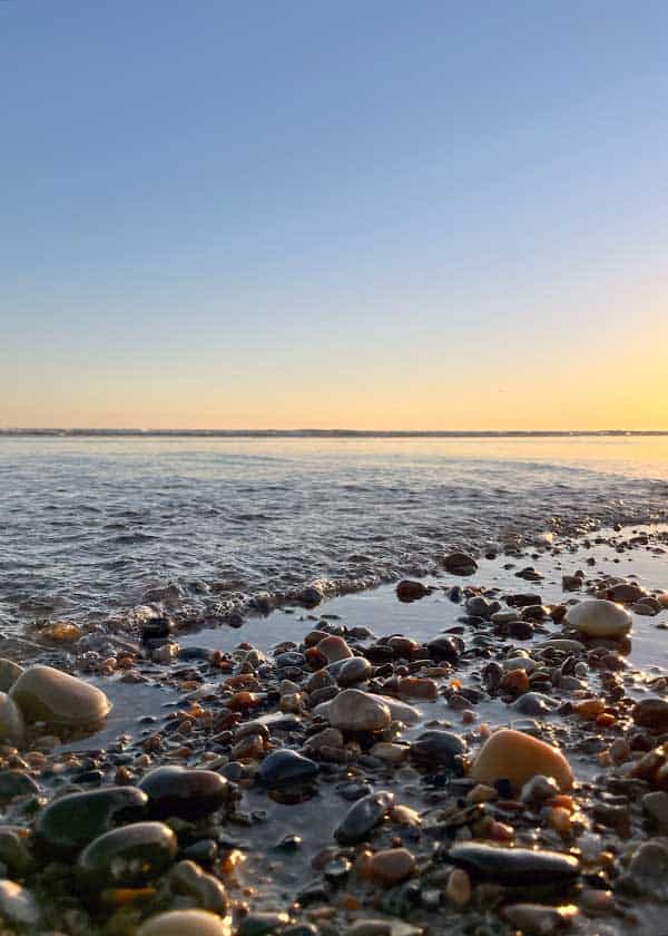 Vandet skvulper let over strandkanten og blandes med de mangefarvede sten på stranden
