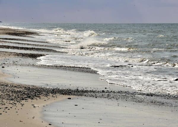 Flot sceneri fra stranden på en rolig dag, bølgerne slår roligt op strandens sten og sand