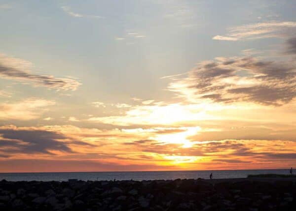 Solnedgang over nordmolen i Hvide Sande - folk går en sen aftentur og nyder at solen går i havet